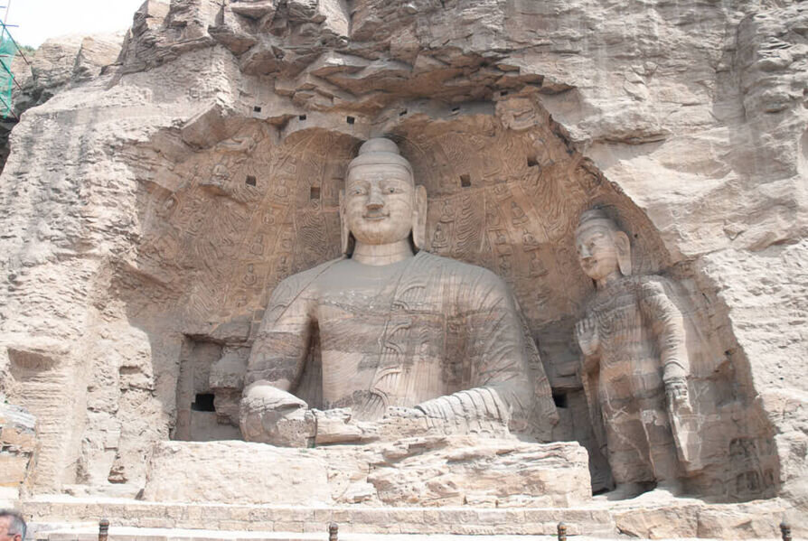 Un buddha seduto all'interno di una grotta con al fianco un altro buddha in piedi più piccolo.