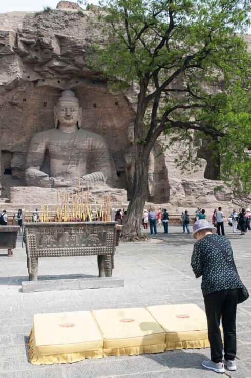 Una donna prega vicino ad un incensiere e davanti alla grande statua di un Buddha scolpito nella roccia.