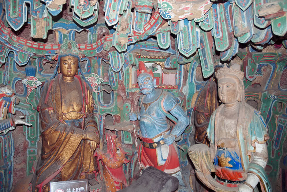 Tre personaggi buddisti all'interno di una grotta colorata e sospesa su una montagna in Cina.