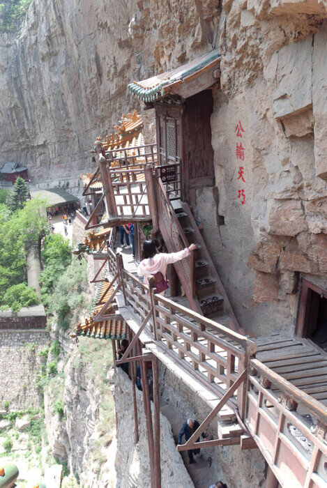 Ragazza scende i gradini di una passerella in legno del tempio sospeso sulla parete di una montagna