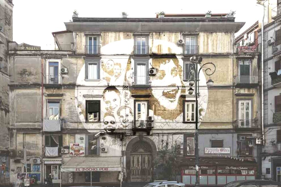 Sulla paerete di un edificio spicca un murale con volti sorridenti e pieni di speranza dei bambini del rione.