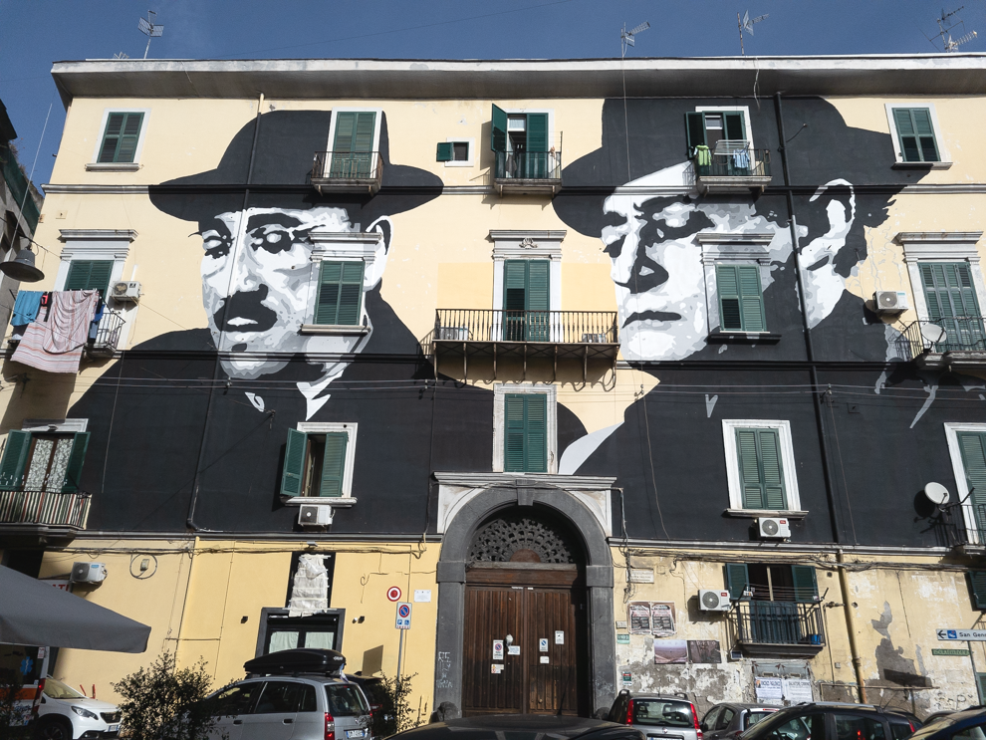 Una intera facciata di un palazzo con un murale dei volti di Totò e Peppino de Filippo a Napoli.