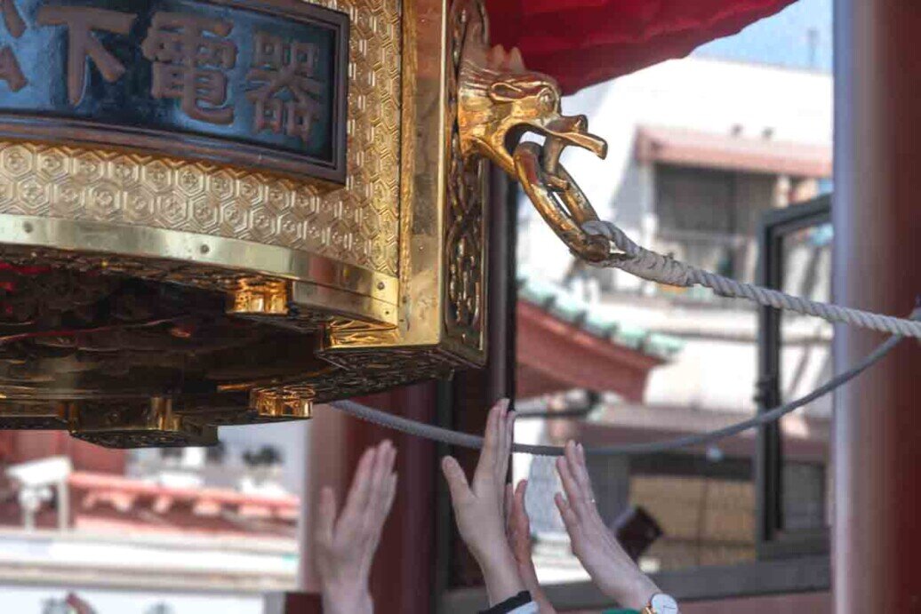 Molte mani dei visitatori si allungano per toccare la lanterna gigante del tempio di Sensō-ji