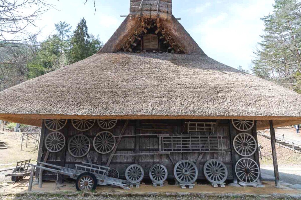 Edificio in legno con grande tetto spiovente e una parete ricoperta da tante ruote per carretti