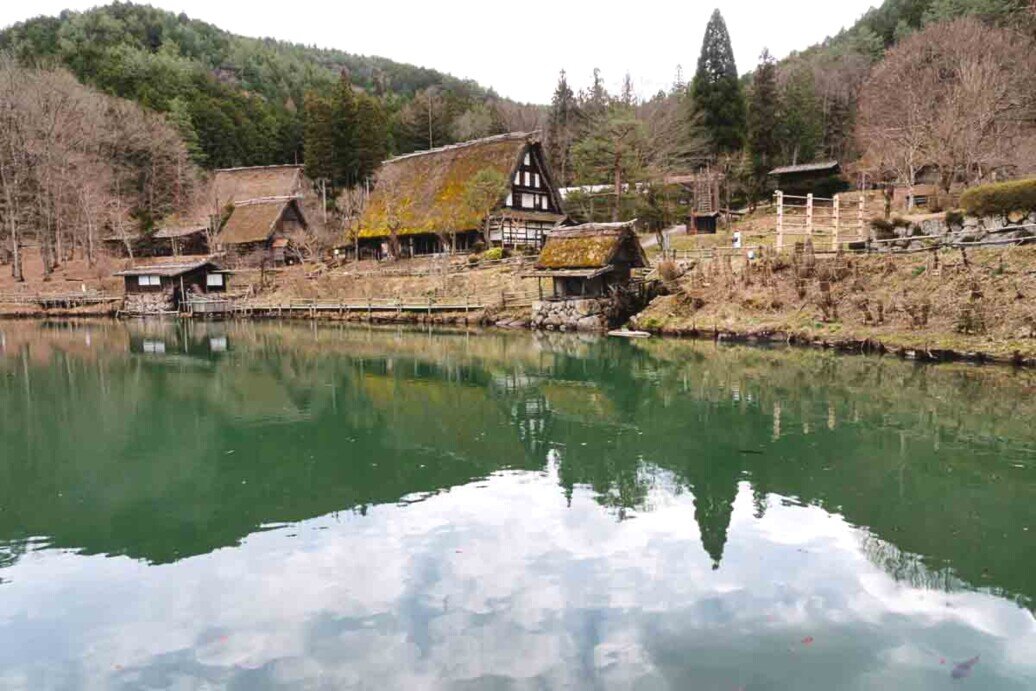 Un lago artificiale su cui si specchiano vecchie case rurali di un museo a cielo aperto all'Hida Folk Village di Takayama