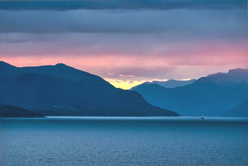 All'alba tra le nuvole una luce solare rende il cielo variopinto le montagne scure e il mare blu notte nel Geirangerfjord