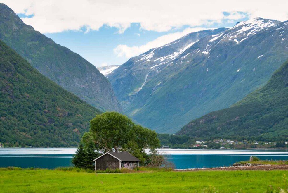 Il lago Oppstrynsvatnet inastonato fra le montagne e gli fa da cornice una piccola casetta rurale.