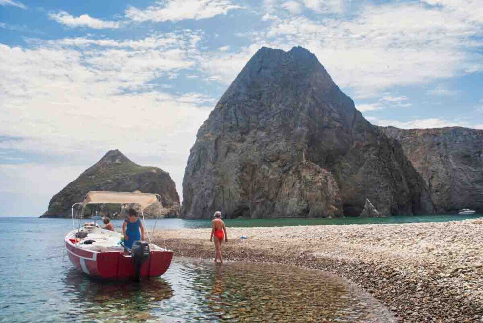 Una barca rossa a motore è approdata su una spiaggia acciotolata con due alti scogli sullo sfondo-nell'Isola di Palmarola.