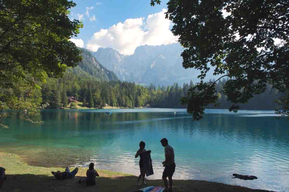 Villeggianti attorno al Lago di Fusine, circondato da montagne.