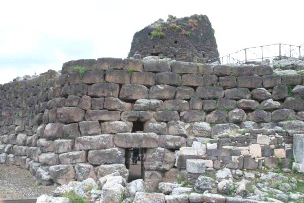 Muro di cinta di pietra con un ingresso, parte dell'architettura della Reggia nuragica di Santu Antine in Sardegna.