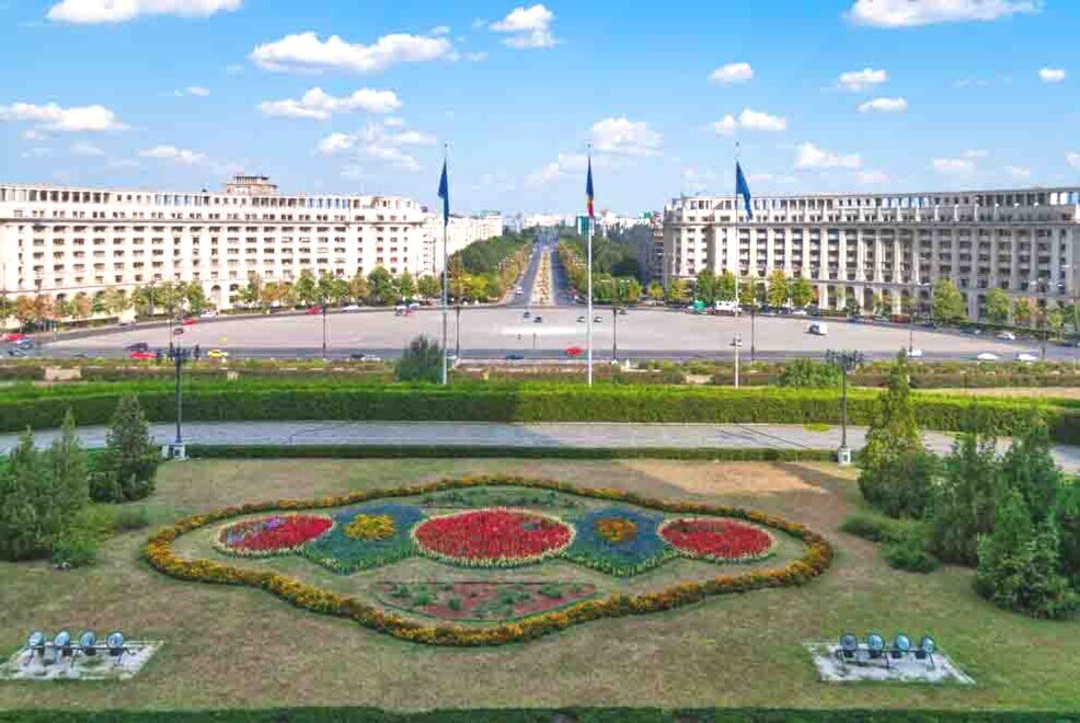 Un giardino e una piazza con aste e bandiere di fronte al Parlamento.