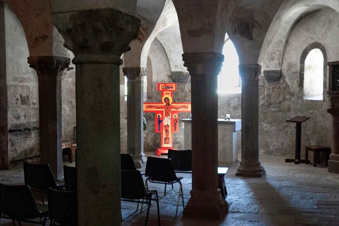 L'interno del Duomo di San Candido all'interno di una cripta con, fra le colonne colonne, un crocefisso rosso.