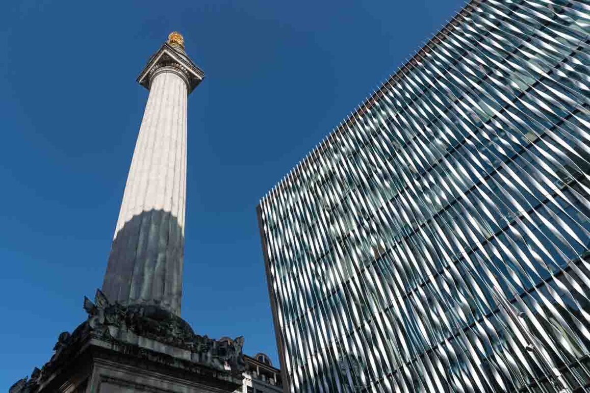 Londra Statua su un alto pilastro con a fianco un grattacelo tutto vetri che riflettono la luce abbagliante del sole.